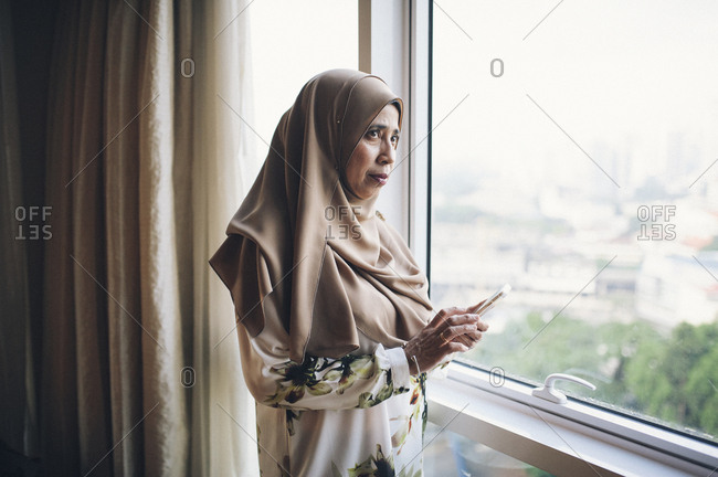 Malaysian woman with phone by window