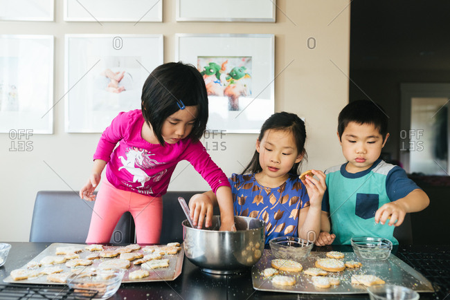 Three children making cookies together at table stock photo - OFFSET