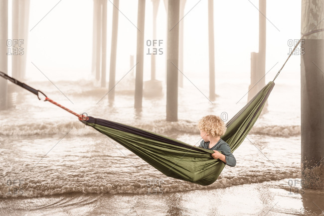 Boy in green hammock under pier in Galveston, Texas