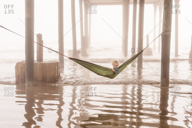 Boy under pier in green hammock in Galveston, Texas