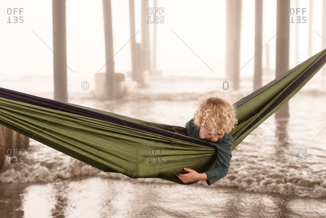 Boy under pier looking over edge of hammock in Galveston, Texas