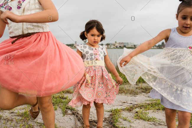 Little girl holding the edge of her skirt while watching her older sisters skip and twirl