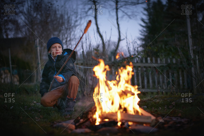 Boy toasting marshmallows on garden campfire at dusk