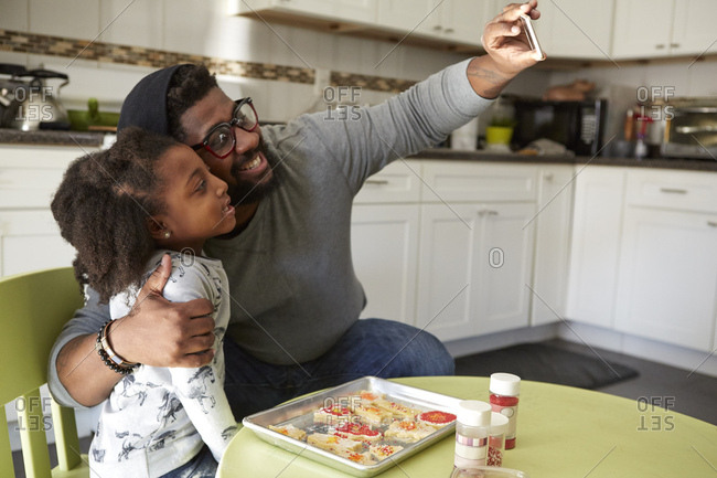 Father and daughter in kitchen, baking, father taking selfie of them both using smartphone