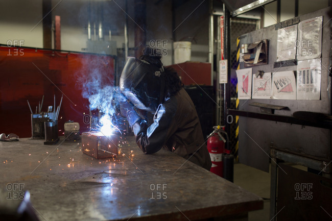 Female metalsmith welding metal box on workbench