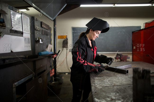 Female metalsmith examining metal rod at workshop bench
