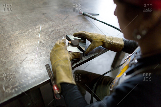 Over shoulder view of female metalsmith aligning metal at workshop bench