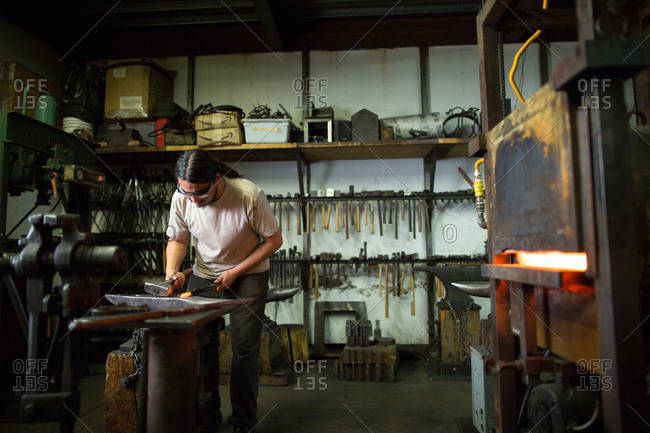 Male metalsmith hammering metal on workshop anvil