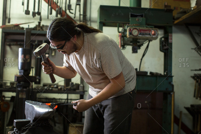 Male metalsmith hammering red hot metal on workshop anvil