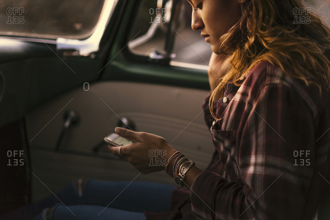 Young woman looking at smartphone in front seat of pickup truck at Newport Beach, California, USA