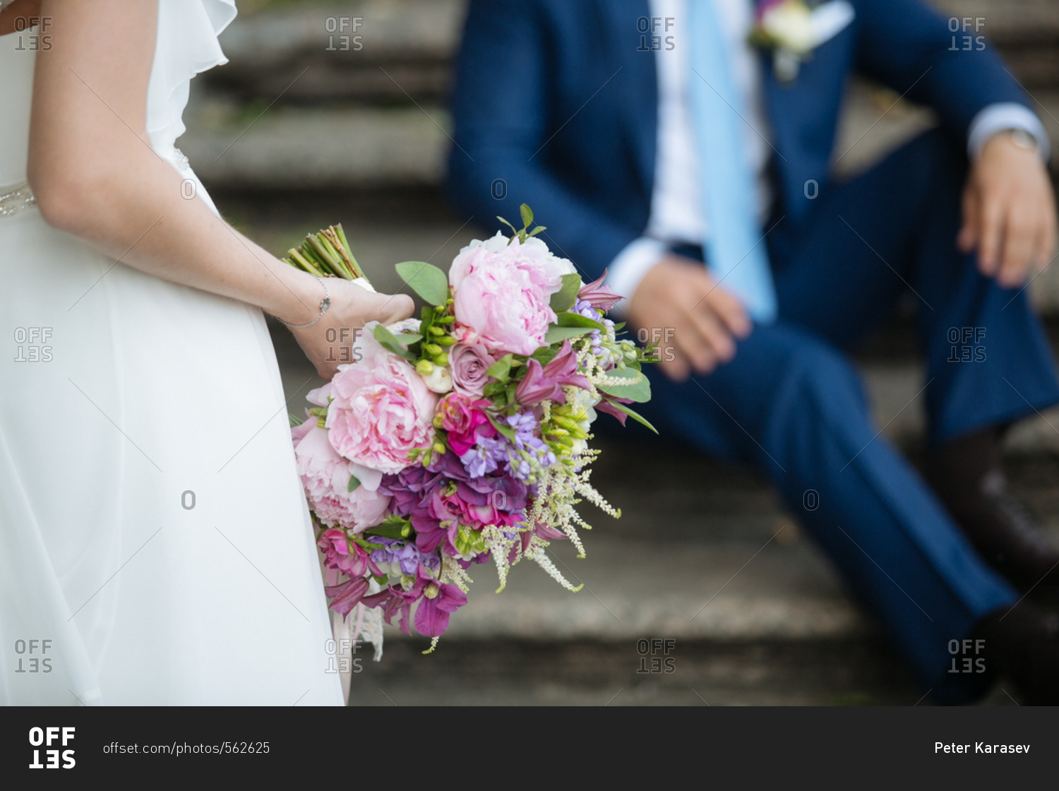 Bride standing in front of her groom holding a bouquet of pink and purple flowers