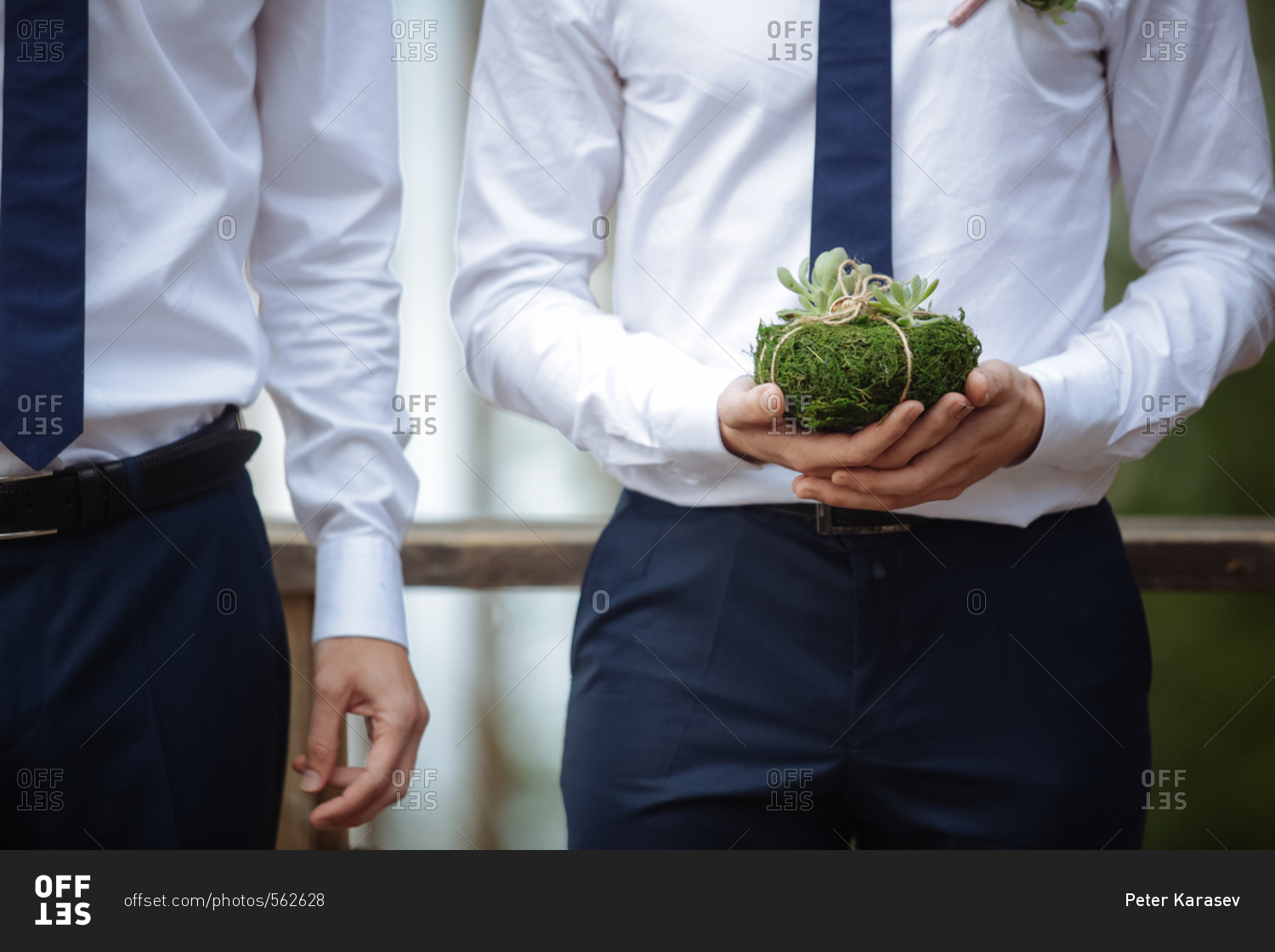Groomsman holding a moss-covered rock with wedding bands