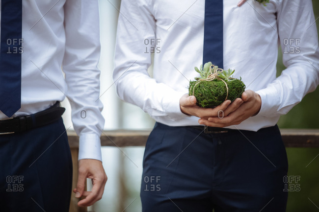 Groomsman holding a moss-covered rock with wedding bands