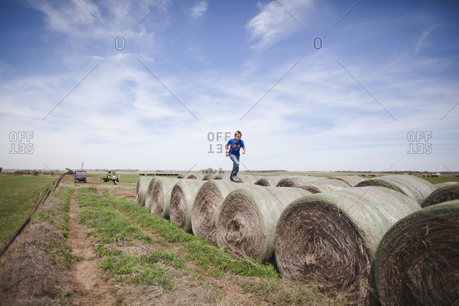 Little boy running across bales of hay on a farm