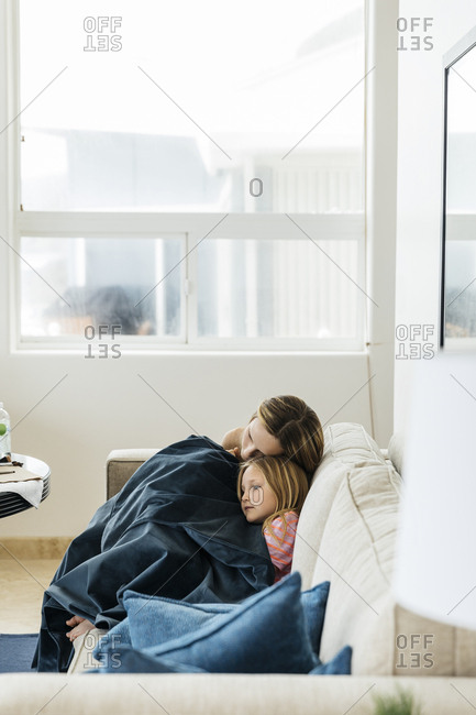 Sisters covered with blanket relaxing on sofa at home