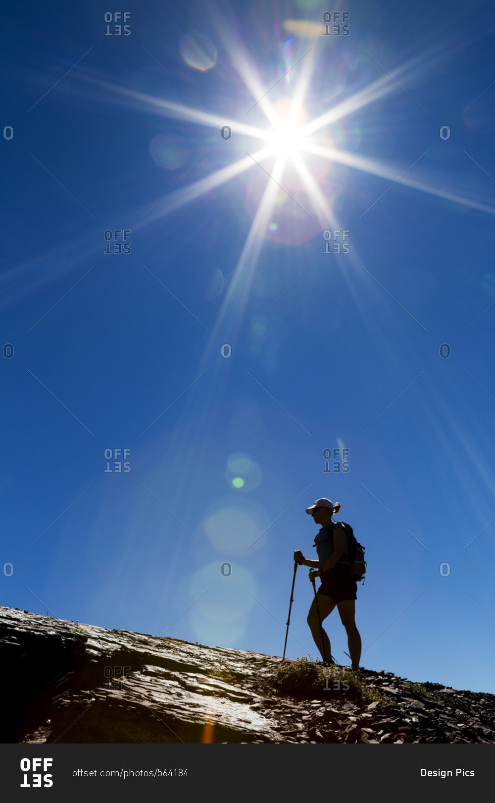 Silhouette of female hiker on rocky ridge with blue sky and sunburst, Waterton, Alberta, Canada