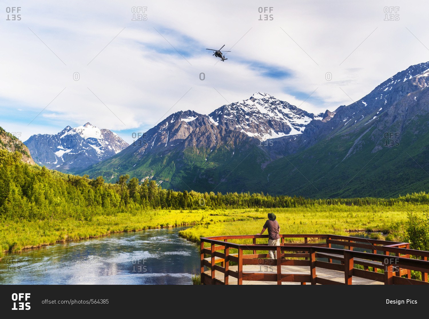 A man is standing on the Eagle River Nature Center boardwalk while a Black Hawk helicopter flies over head in the Chugach State Park in South-central Alaska, USA