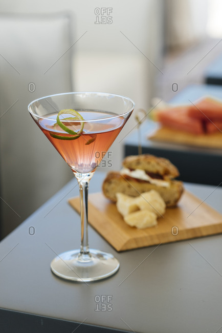 Pink cocktail with lime rind garnish served with sandwich