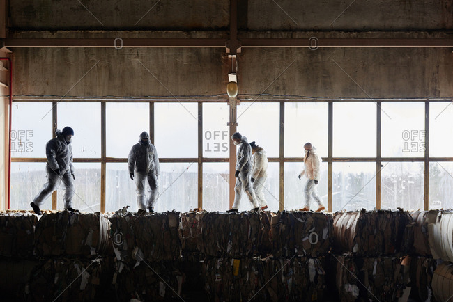 Waste sorters in protective wear walking on top of compressed cardboard blocks at garbage recycling plant