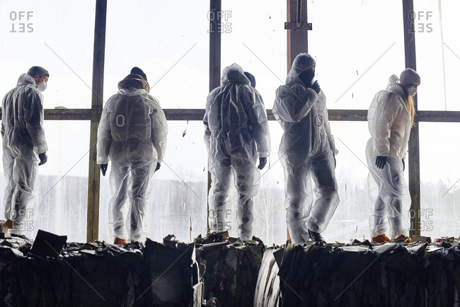 At garbage recycling plant. Conceptual shot of waste operatives in protective uniform standing on bales of compressed cardboard against large window background