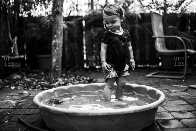 Toddler girl in wet clothes standing in a kiddie pool and looking down