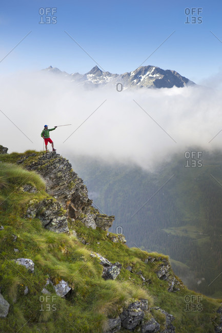 Hike on steep ridge pointing with hiking pole with mountain range in background