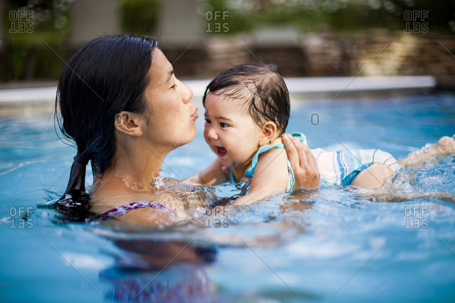 A Japanese American mother swims and holds her 10 month old baby girl in a swimming pool.