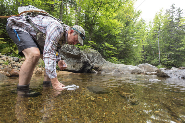 A Fly Fisherman Gathering A Sample Of Freshwater To Test For The Presence Of Microplastics
