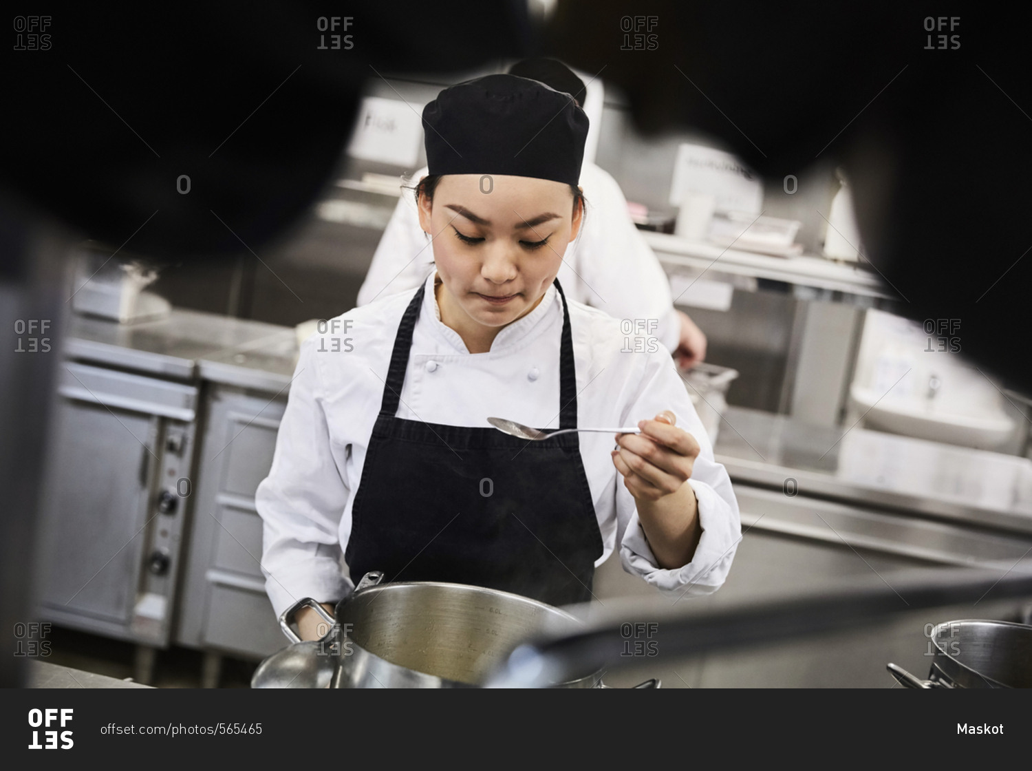 Young female chef tasting food from cooking pan at commercial kitchen