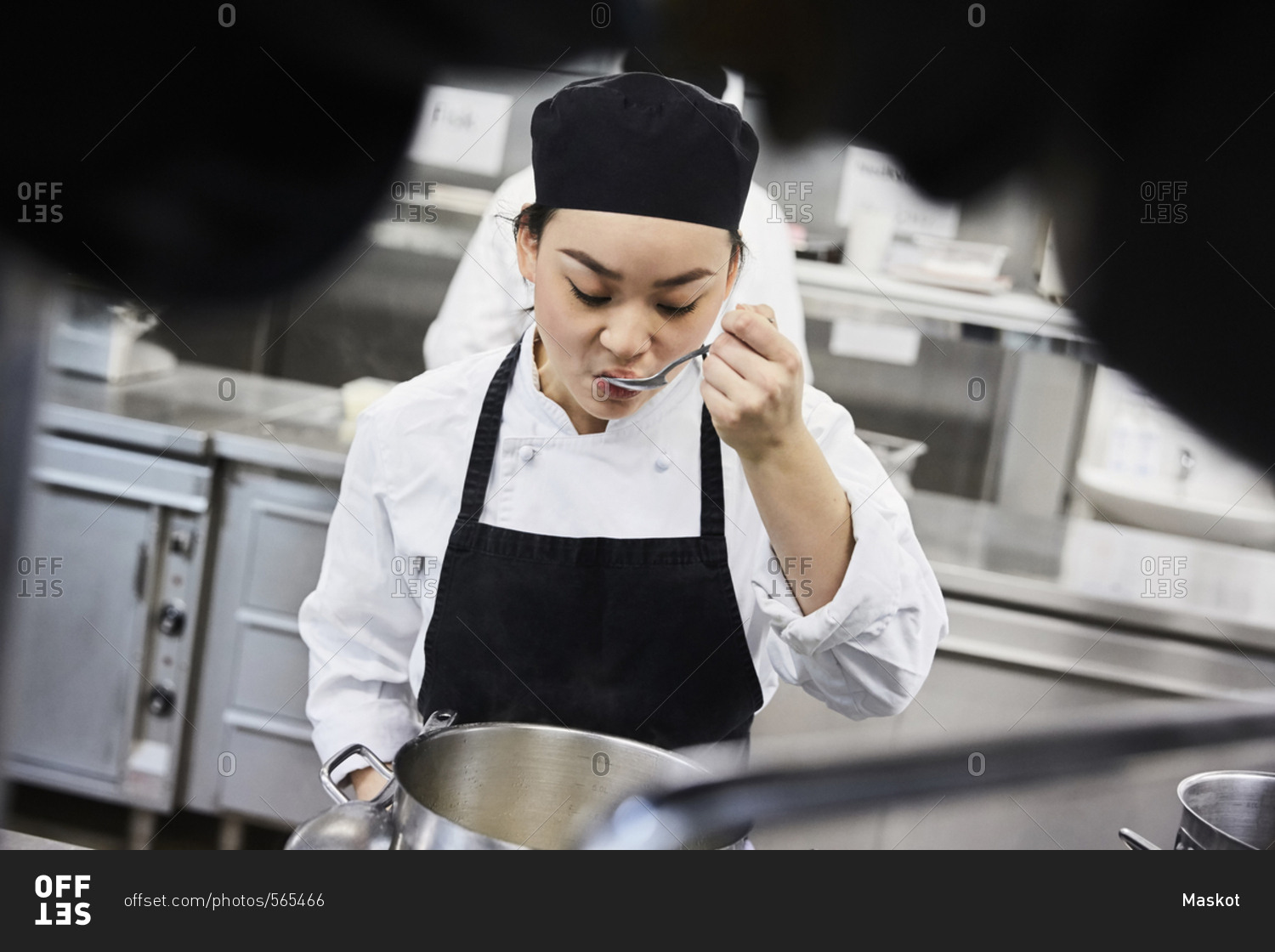 Female chef tasting food from cooking pan at commercial kitchen