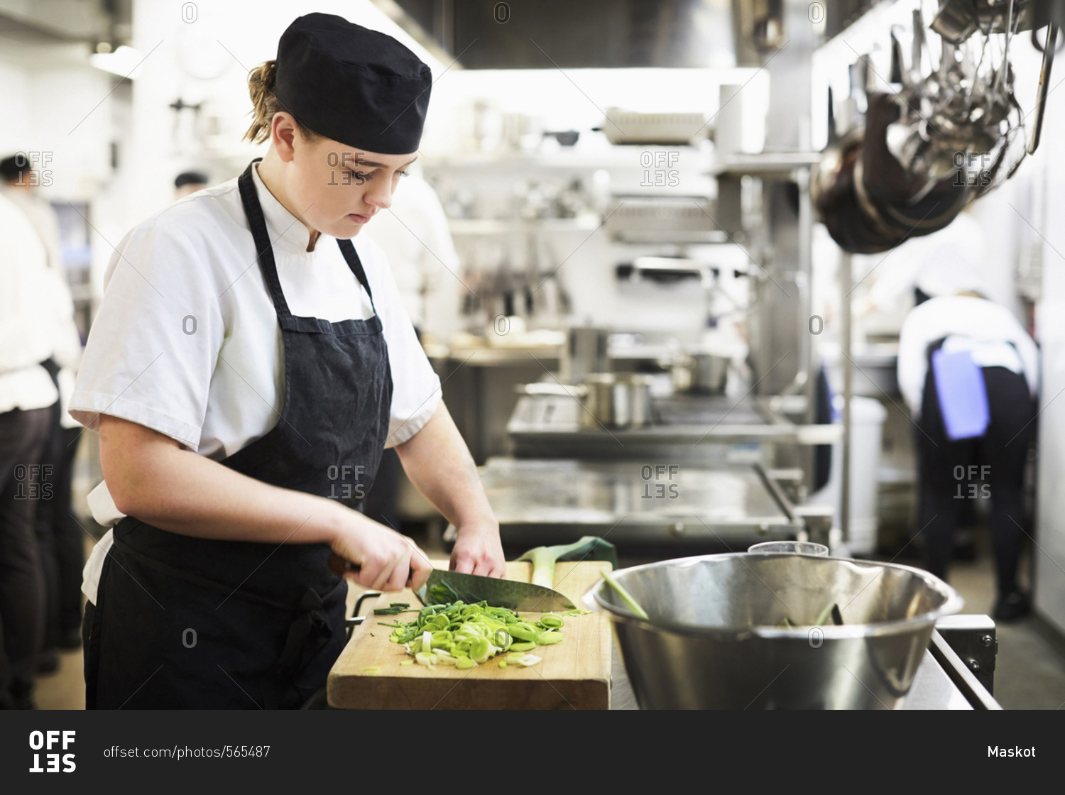 Young female chef chopping vegetables on cutting board in cooking school