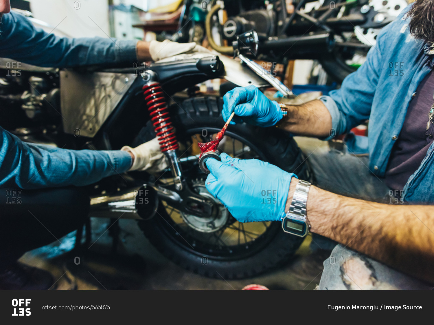 Two mature men, working on motorcycle in garage, close-up