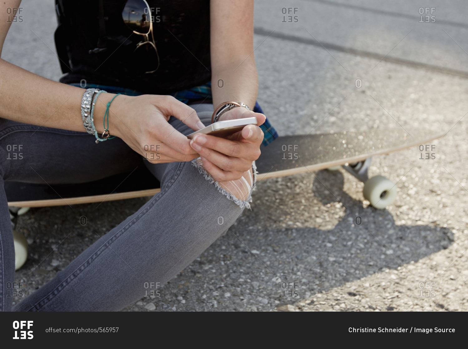 Mid section of female skateboarder sitting on skateboard texting on smartphone