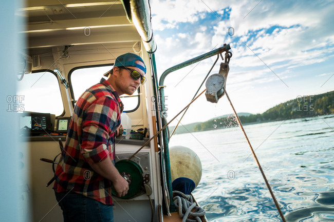 Young man raising winch on fishing boat on coast of Maine, USA