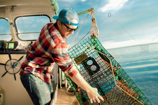 Young man lifting lobster cage from winch on fishing boat on coast of Maine, USA
