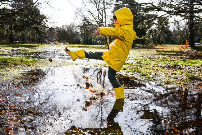Boy in yellow anorak splashing in park puddle