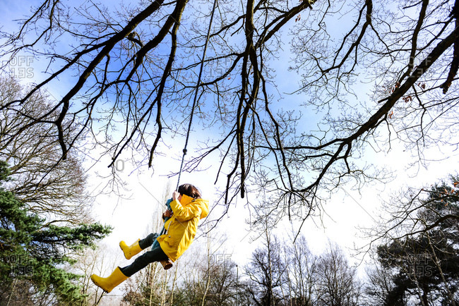 Boy in yellow anorak swinging from park tree