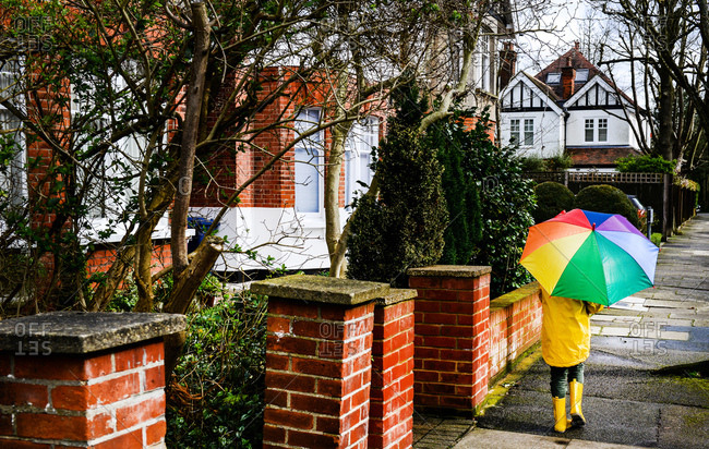 Rear view of boy in yellow anorak carrying umbrella along street