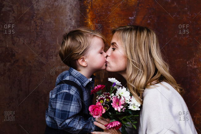 Young boy giving bunch of flowers to mother, mother kissing boy