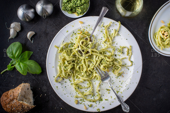 A devoured plate of pesto pasta with ingredients surrounding plate and a glass of white wine, overhead view