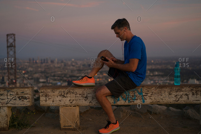 Jogger sitting on bench looking at smartphone, Runyon Canyon, Los Angeles, California, USA