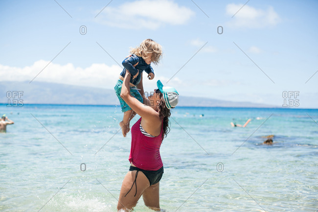 Woman standing in sea, lifting son in air