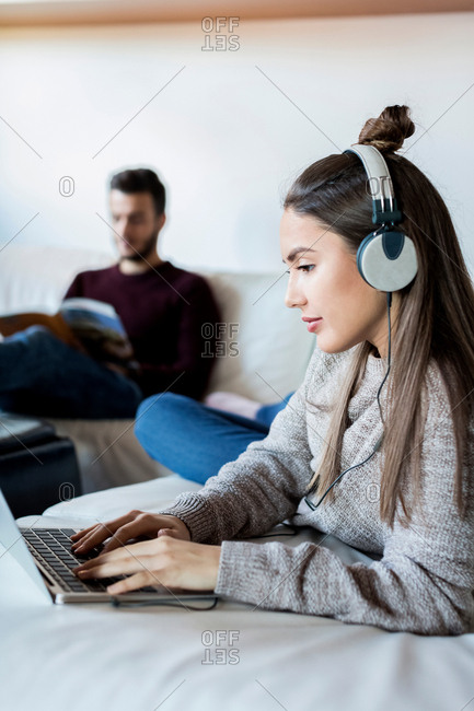 Young couple relaxing at home, young woman using laptop, young man reading magazine