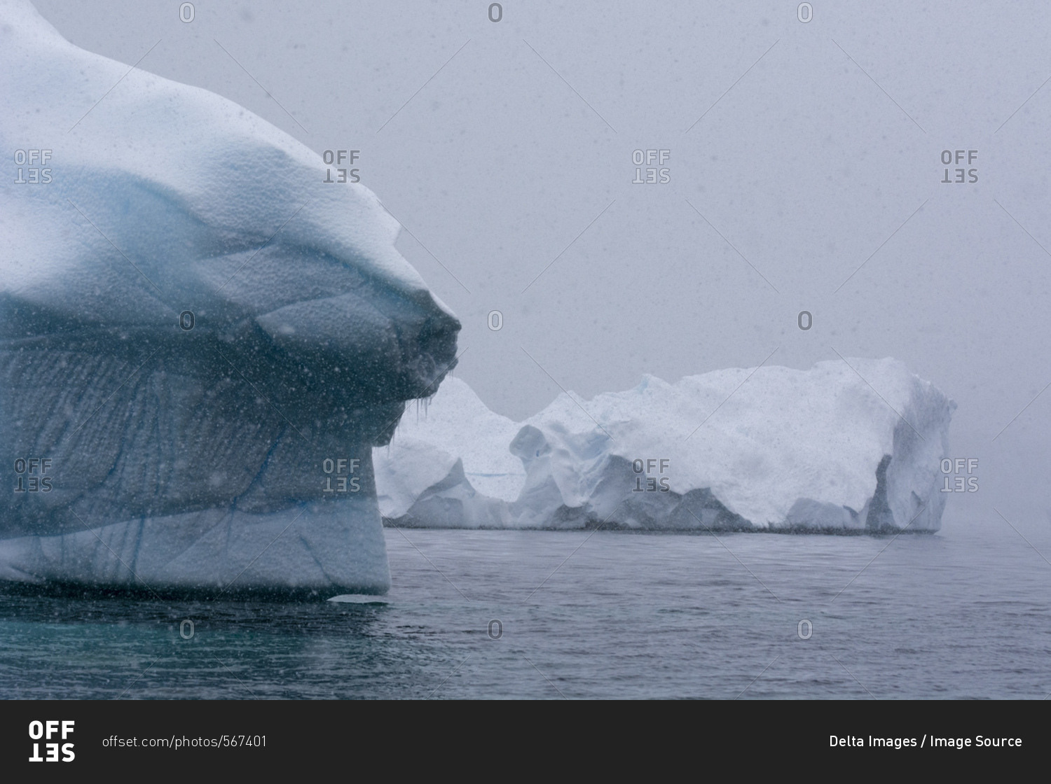Snowfall over icebergs in Portal Point, Antarctica stock photo - OFFSET