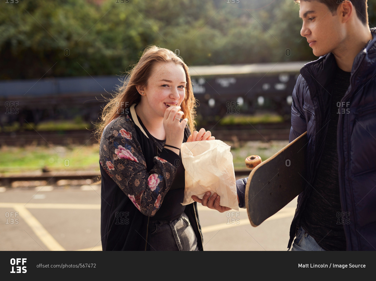 Young man sharing bag of chips with young woman,  skateboard under young man\'s arm, Bristol, UK