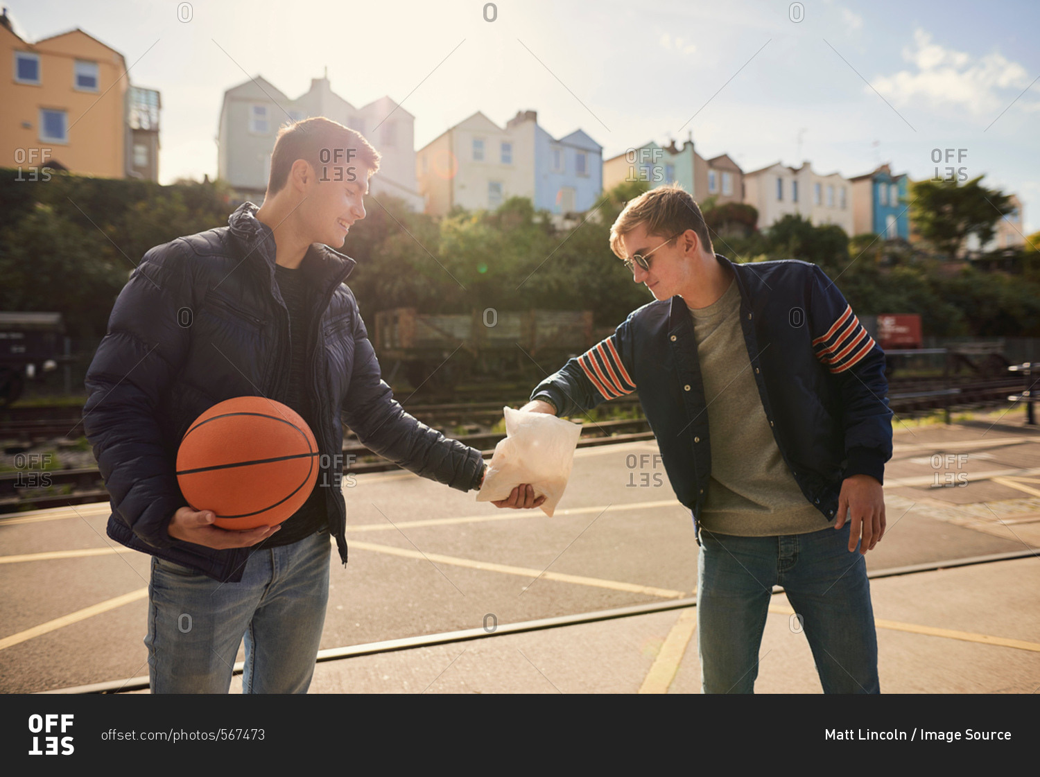 Young man sharing bag of chips with friend, young man holding basketball, Bristol, UK