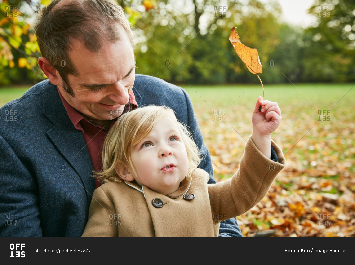 Daughter sitting on father's lap holding autumn leaf