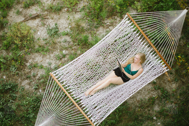 Overhead view of young woman looking at digital tablet on hammock at beach