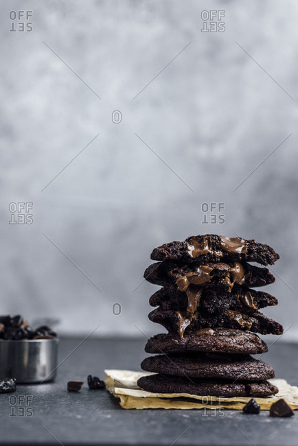 A stack of Mexican hot chocolate cookies photographed from front view. Chocolate chips in the cookies are melting. A cup of chocolate chips accompany.