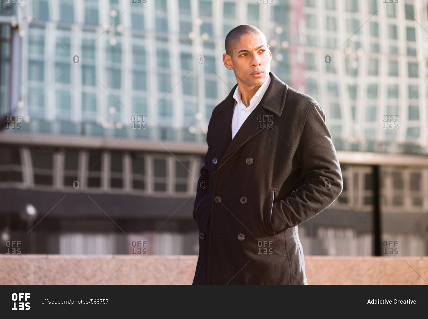 Cool young man wearing coat holding hands in pockets and looking away. Horizontal outdoors shot.